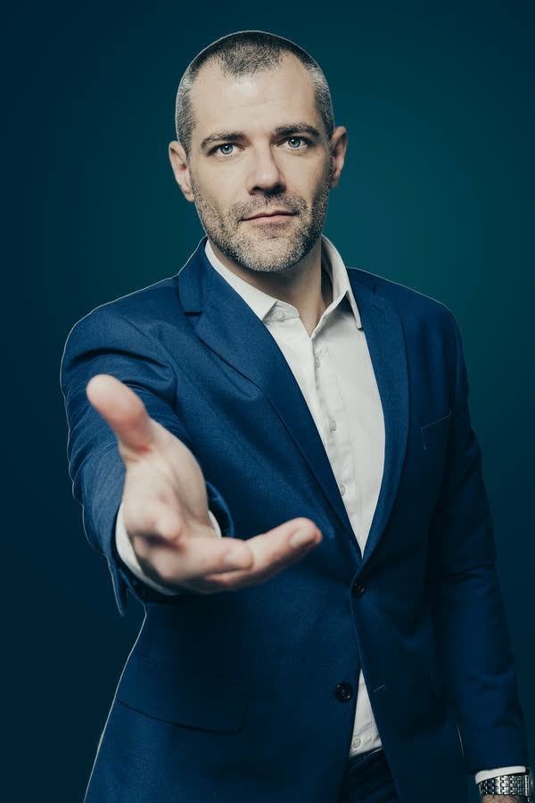 Roberto Monfort de terno azul, estendendo a mão aberta em direção a quem olha